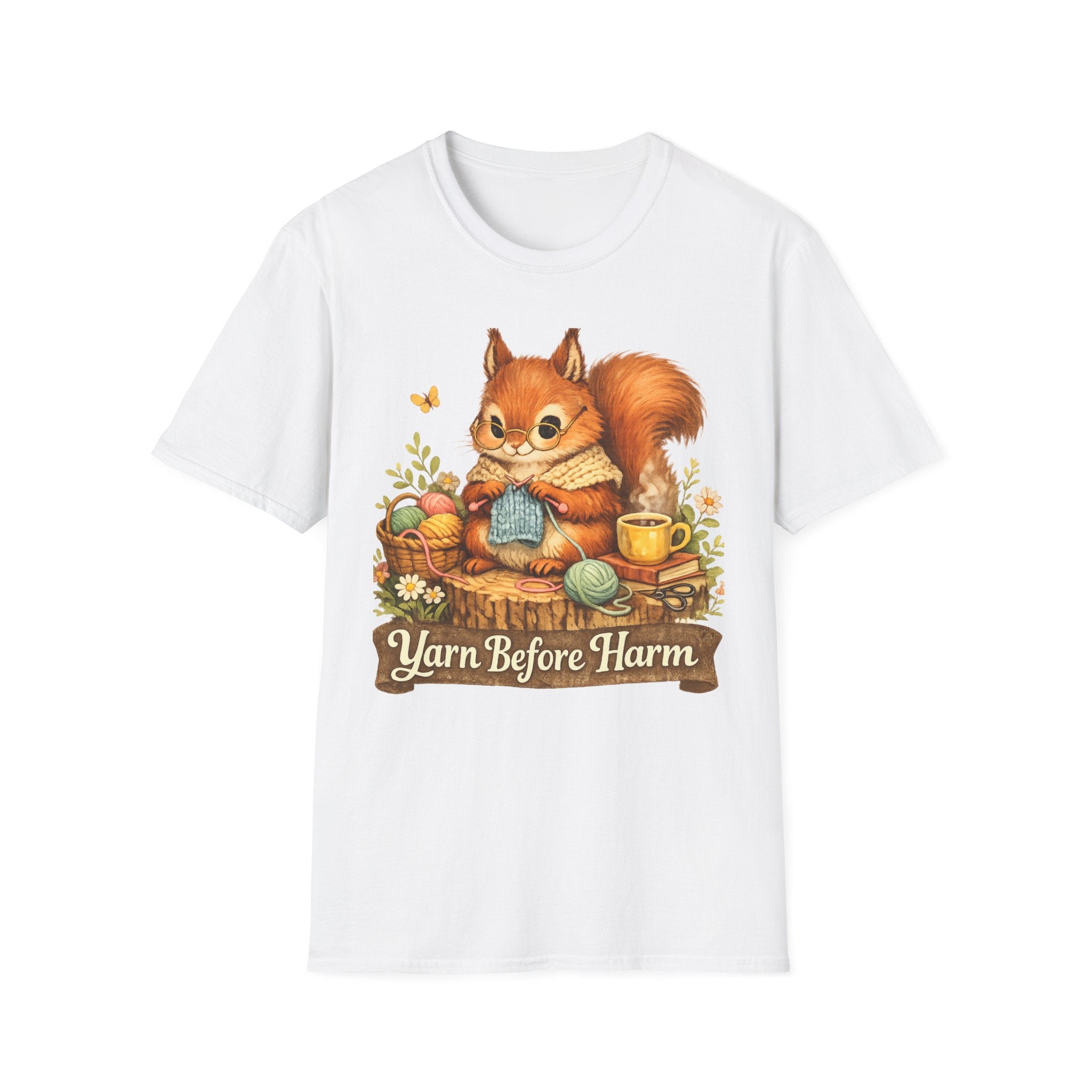 A white short-sleeve crewneck t-shirt featuring a colorful graphic of a red squirrel knitting a blue sweater with yarn, surrounded by flowers and a banner that reads 'Yarn Before Harm'.