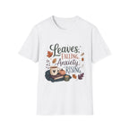A white short-sleeve crewneck t-shirt featuring a graphic print with the text 'Leaves, Falling, Anxiety Rising' in a mix of black and reddish-brown fonts, surrounded by autumn-themed illustrations including leaves, a mug, a pumpkin, and a candle.