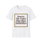 A white short-sleeve crewneck t-shirt with a graphic print on the front. The print features a gold-bordered square containing the text 'Sorry, My Face Has Has Subtitles And They Are Not Rated G' in dark brown lettering.