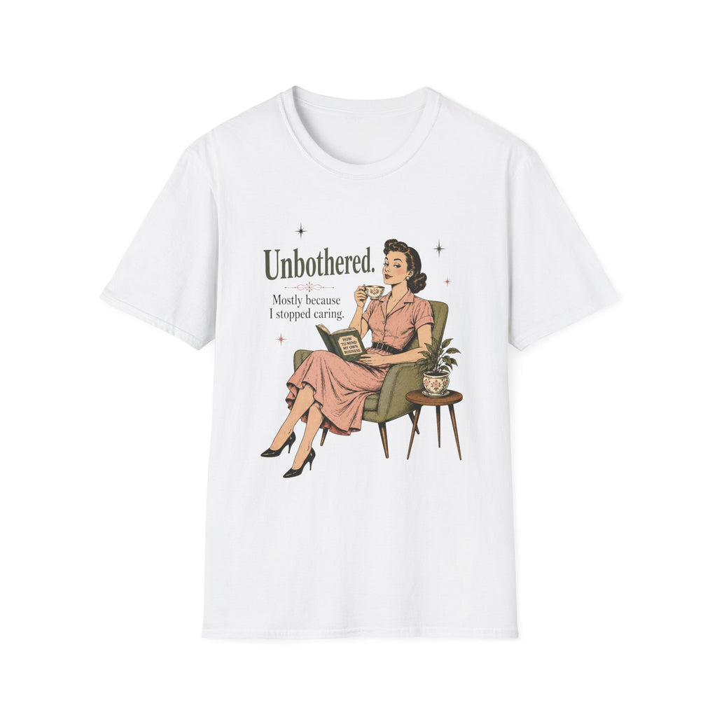 A white short-sleeve crewneck t-shirt featuring a retro-style graphic of a woman in a pink dress sitting in an armchair, with the text 'Unbothered. Mostly because I stopped caring.