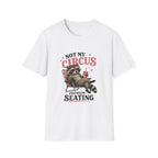 A white short-sleeve crewneck t-shirt featuring a graphic print of a raccoon sitting in a red chair with the text 'NOT MY CIRCUS PREMIUM SEATING'.