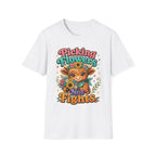 A white short-sleeve crewneck t-shirt featuring a colorful graphic print of a cartoon cow wearing a flower crown and holding sunflowers, surrounded by the text 'Picking Flowers Not Fights' in playful multicolor lettering.
