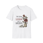 A white short-sleeve crewneck t-shirt featuring a vintage-style graphic print on the front with the text 'YOU WERE A LESSON. NOT A SOULMATE.