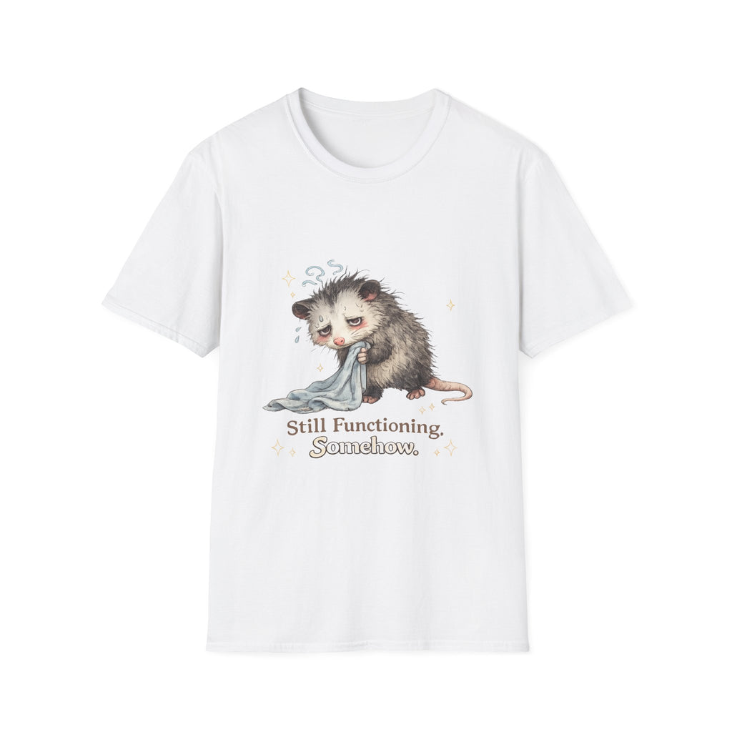 A white short-sleeve crewneck t-shirt featuring a graphic of a sad, sleepy opossum holding a blanket, with the text 'Still Functioning, Somewhere.' printed below it.